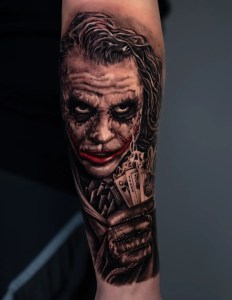 Realistic black and grey Joker portrait tattoo with detailed shading and color highlights, done at Monochrome Tattoo Studio in Fresno.